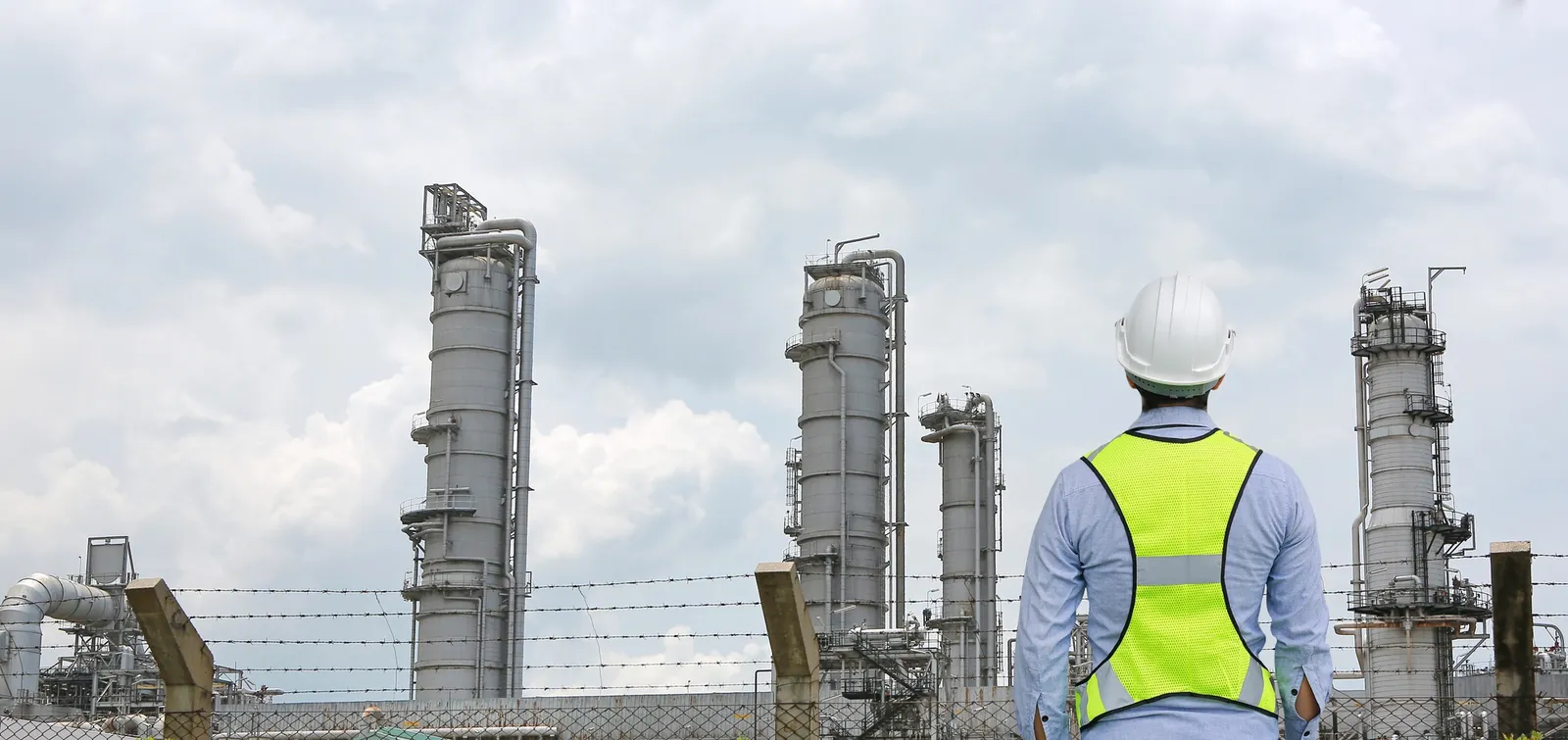 Técnico con chaleco de seguridad frente a una planta industrial.
